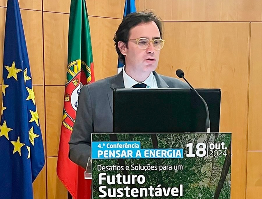 Nelson Lage com fato escuro e óculos fala ao púlpito durante a 4.ª Conferência Pensar a Energia. À frente do púlpito, há um cartaz do evento com os dizeres: “Desafios e Soluções para um Futuro Sustentável – 18 out. 2024”. Ao fundo, estão visíveis as bandeiras da União Europeia, de Portugal e da Universidade do Algarve.