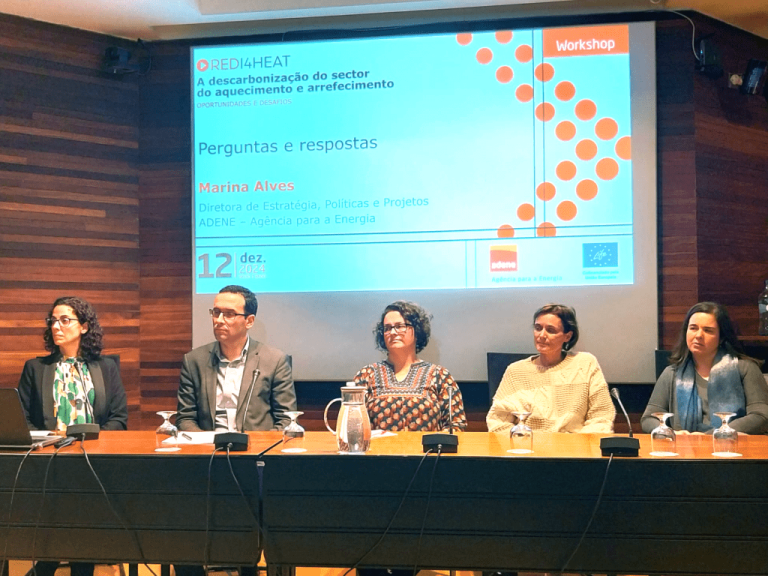 Cinco pessoas estão sentadas lado a lado atrás de uma mesa longa, participando num painel de discussão. Atrás delas, é projetado um slide com o título do workshop: “REDI4HEAT – A descarbonização do sector do aquecimento e arrefecimento: Oportunidades e Desafios”. O slide indica que a sessão é de “Perguntas e respostas” com Marina Alves, Diretora de Estratégia, Políticas e Projetos da ADENE – Agência para a Energia. O evento decorre no dia 12 de Dezembro de 2024. Também aparecem os logótipos da ADENE e da União Europeia.