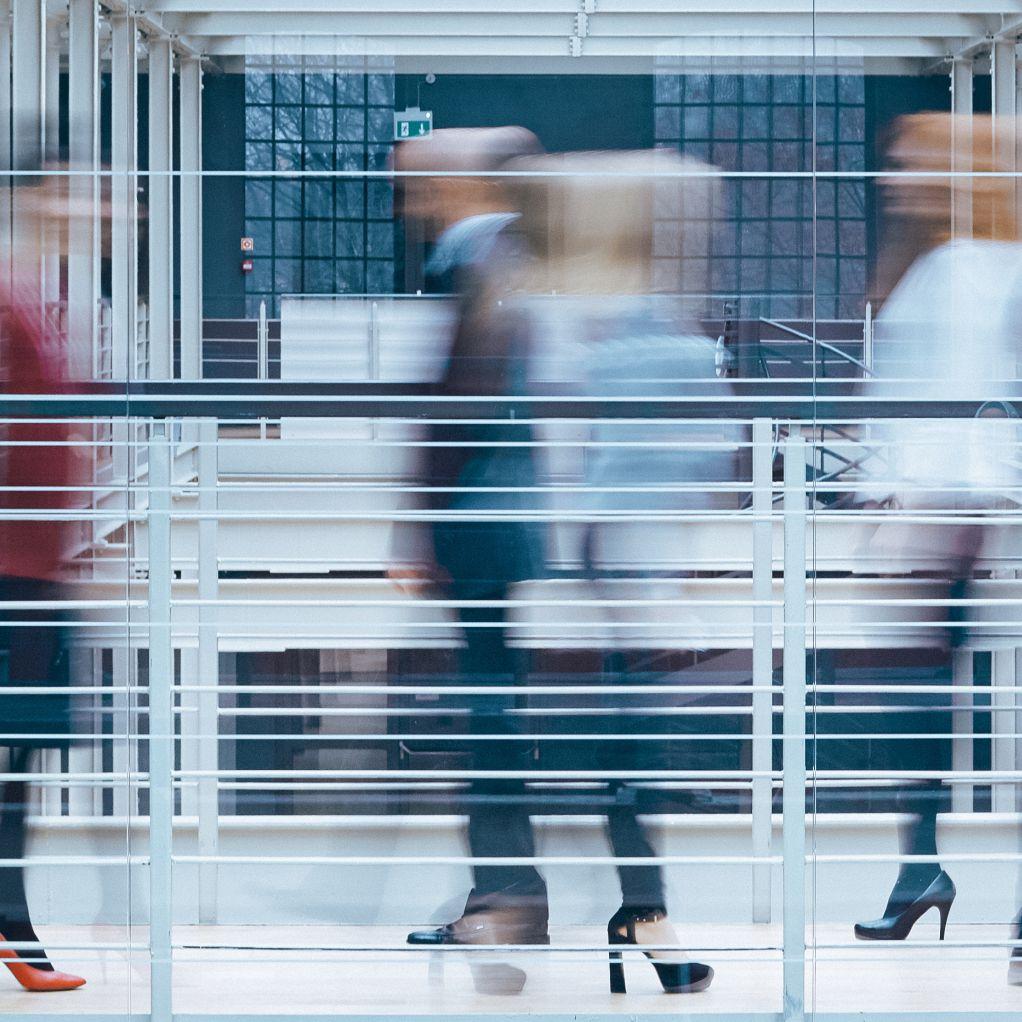 Imagem desfocada com pessoas a circular num corredor de um edifício de comércio ou serviços